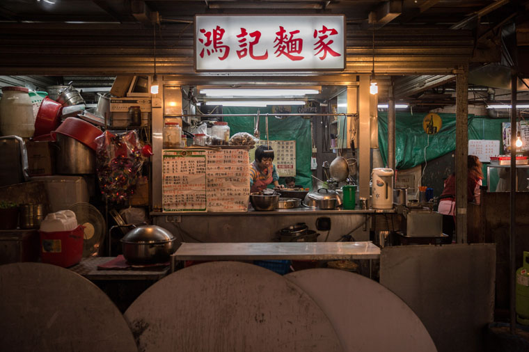 TO GO WITH Lifestyle-HongKong-China-food-culture,FEATURE by Justine Gerardy In this picture taken during the evening on April 9, 2015, an employee (C) serves food at a "dai pai dong" street food stall in the Sham Shui Po district of Hong Kong. Offering the rare chance to eat outdoors, escaping the Asian financial hub's air-conditioned high-rises, the eateries are a nostalgic throwback to Hong Kong's past.  With no walls, cooks in the open, customers on plastic stools, melamine plates and bunches of chopsticks in tabletop jars, its a no-fuss formula that still draws customers day and night.      AFP PHOTO / ANTHONY WALLACE